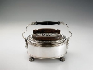 silver warmer of oval shape standing on four paw feet. Plain body, pierced lid with double wood handles.Swivelling double scroll handle with central ebonized wood support